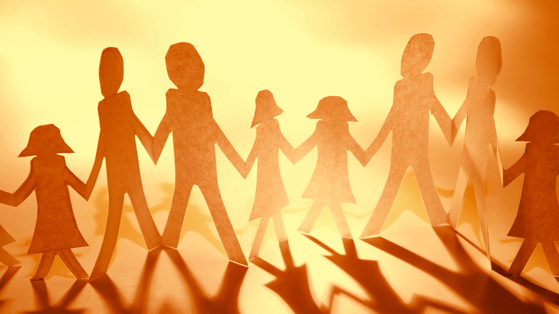 Paper cut-out figures holding hands in a row, casting long shadows in warm light