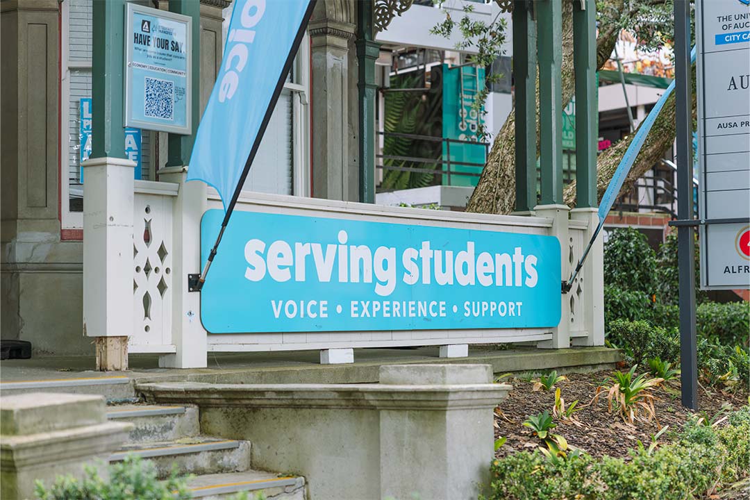 A banner outside the AUSA building that says 'serving students' in white text on a blue background