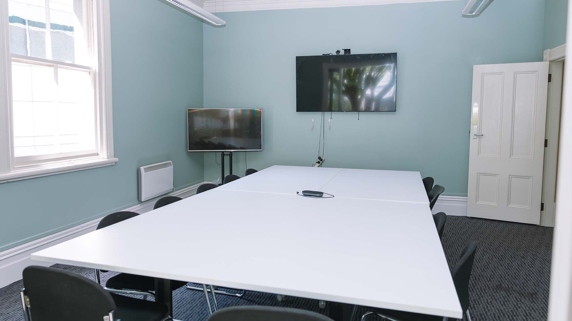 An empty meeting room with a large white table in the middle and a tv mounted on the wall