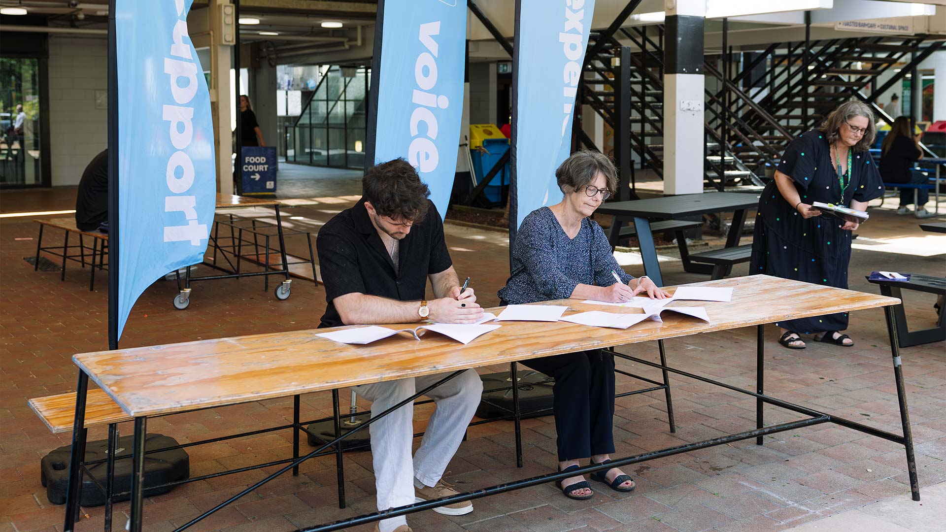 Two staff members sat at a lng wooden table writing papers