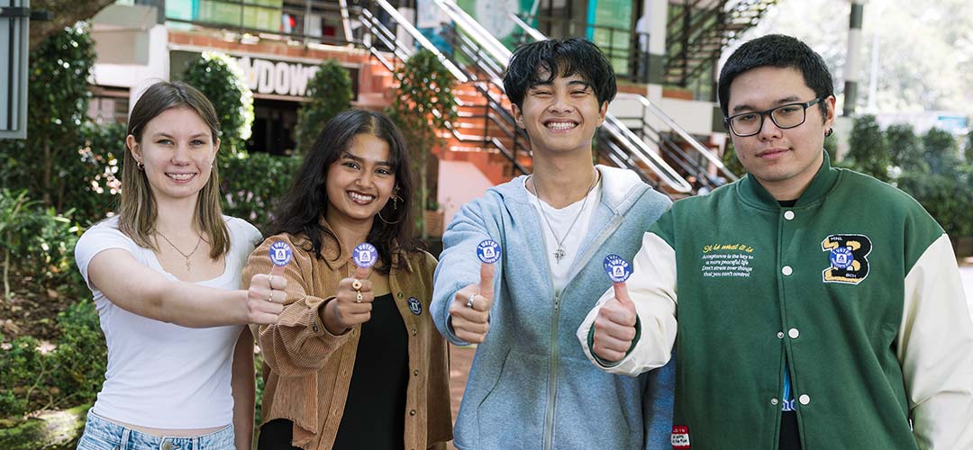 Students with little voting stickers stuck to their thumbs while they smile at the camera